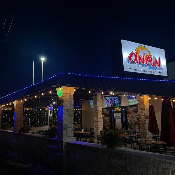 Cancun Mexican Restaurant & Seafood at night, with a lit sign, patio seating, and string lights.
