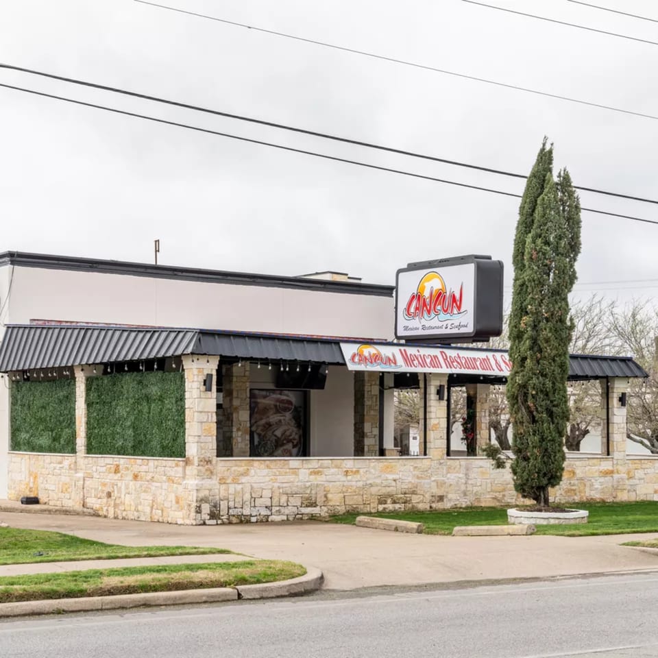 Exterior of Cancun Mexican Restaurant, a stone building with a black awning and prominent signage.