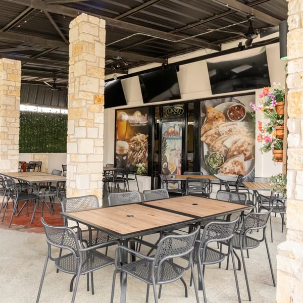 Outdoor patio seating at Cancun Mexican Restaurant with stone pillars and large window decals.