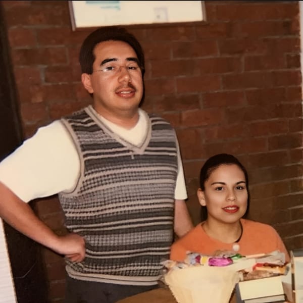 Two people, a man in a striped vest and a woman in an orange shirt, smiling at the camera.