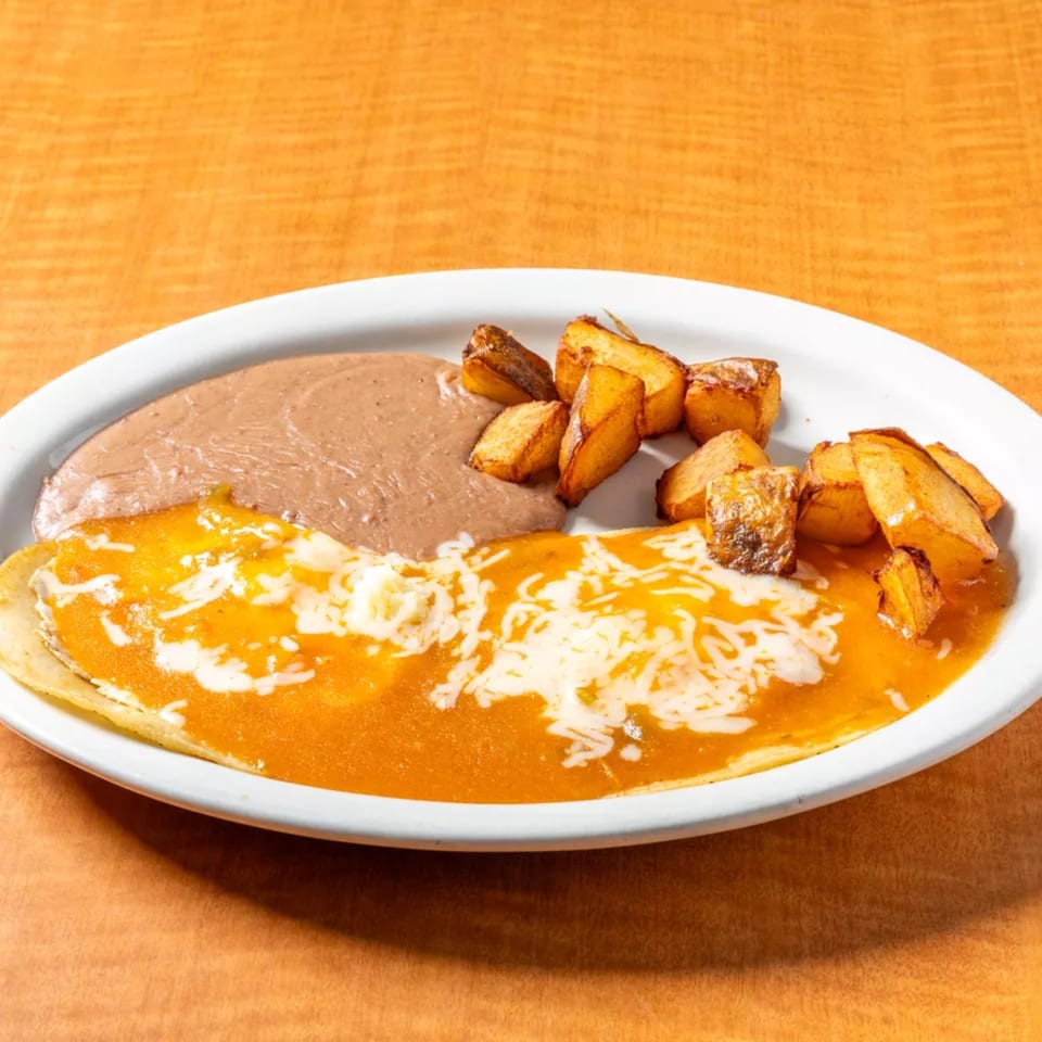 Huevos Rancheros with refried beans and home fries on a white plate from Cancun Mexican Restaurant.
