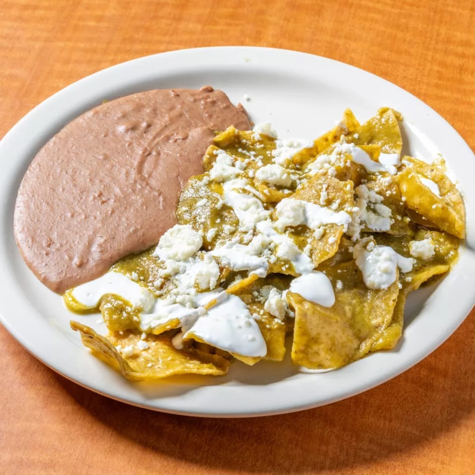Chilaquiles with green sauce, sour cream, and cotija cheese, served with refried beans.