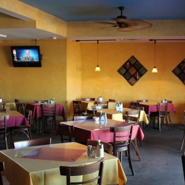 Interior of Cancun Mexican Restaurant with yellow walls, red and yellow tablecloths, and a TV showing a news anchor.
