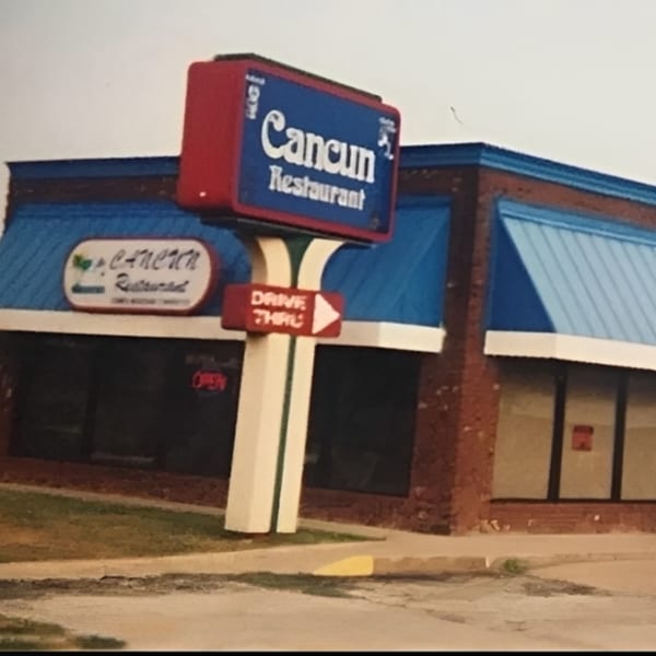 Exterior of Cancun Mexican Restaurant with a large blue and red sign and blue awnings.