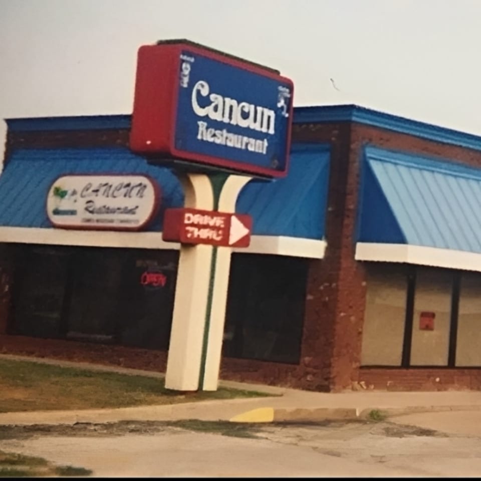 Exterior of Cancun Mexican Restaurant with a large blue and red sign and blue awnings.